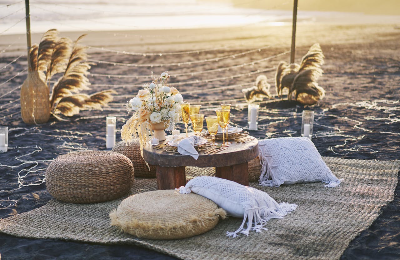 Luxurious beachside picnic with cushions, glassware, and decor in sunset light.
